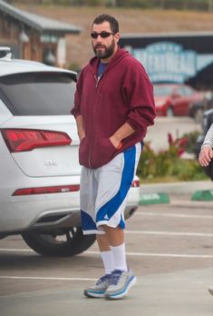 a man walking across a parking lot next to a white car