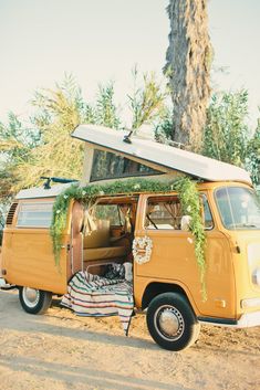 an old vw van with a surfboard on the roof is parked in front of a palm tree