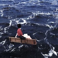 a man sitting on top of a wooden bench in the middle of some ocean waves