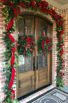 a decorated front door with christmas wreaths and red ribbons on it's sides