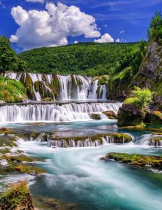 the waterfall is surrounded by green trees and blue water, with clouds in the sky