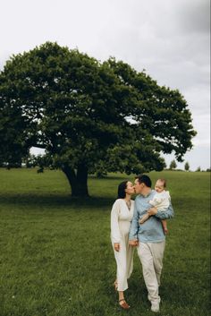 a man and woman kissing while holding a baby in front of a large green tree