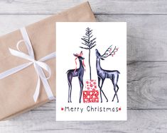 a christmas card with two deers and a present on the table next to it