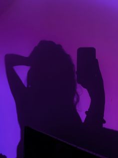 the silhouette of a woman holding a cell phone up to her head in front of a purple background