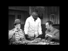 three men are sitting at a table with plates and drinks in front of them, one is wearing a top hat