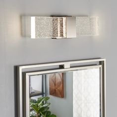 a bathroom mirror sitting on top of a white wall next to a potted plant