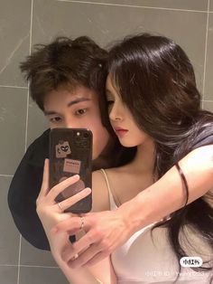 a man and woman taking a selfie in front of a bathroom mirror with their cell phone