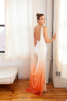 a woman standing in front of a window wearing an orange and white dress with sheer drapes