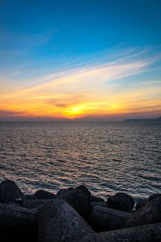 the sun is setting over the ocean with rocks