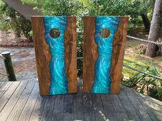 two pieces of wood with blue designs on them sitting on a wooden deck in front of some trees