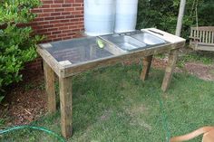 a dog laying on the grass next to a table with two water tanks and a sink