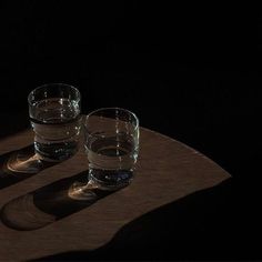 two glasses sitting on top of a wooden table next to each other in the dark