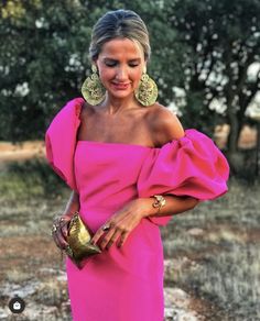 a woman in a pink dress is standing outside wearing large gold earrings and holding a purse