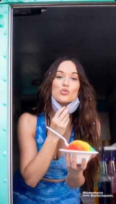 a woman in a blue dress is holding a bowl and eating something out of a container