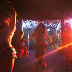 several people dancing in the dark under a tent with bright light coming from behind them