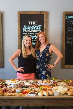 two women standing in front of a table full of food