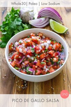 a white bowl filled with salsa next to cilantro, onions and lime wedges