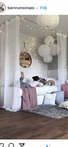 a person laying on a bed in a room with white curtains and lights hanging from the ceiling