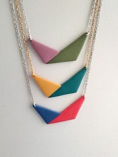 three necklaces with different colored triangles hanging from chains on a white surface and one has a gold plated chain