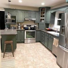 a kitchen with green cabinets and stainless steel appliances, including an oven, refrigerator, microwave, dishwasher, sink, and stool