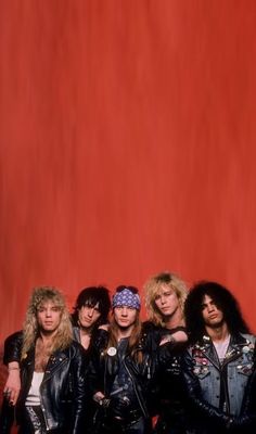 the group of rockers posing for a photo in front of a red wall with their arms around each other