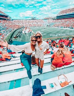 two women sitting on the bleachers in front of an audience at a football game