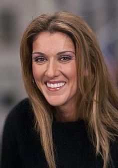 a smiling woman with long hair and brown eyeshadow, wearing a black sweater