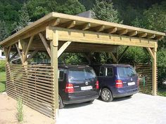 two cars are parked under a wooden shelter