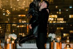 a man and woman kissing on top of a building with candles in front of them