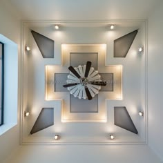 a clock mounted to the ceiling in a room with white walls and recessed lighting