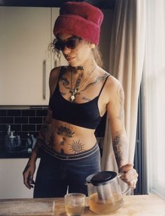 a woman with tattoos on her stomach standing in front of a counter holding a teapot