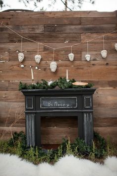 an old fireplace is decorated with greenery and candles for the holiday season in front of a wooden wall