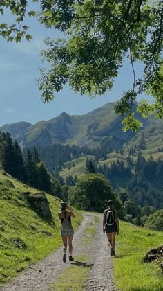 two people walking down a dirt road in the mountains