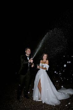 a bride and groom standing in the rain with their arms around each other as they spray champagne into the air