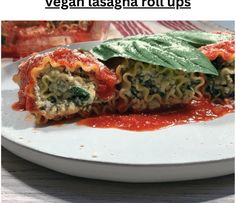 a white plate topped with lasagna rolls covered in sauce and spinach leaves