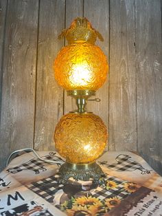 a yellow glass lamp sitting on top of a table next to a wooden wall behind it