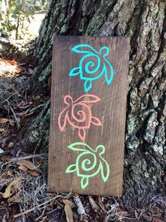 a wooden sign sitting next to a tree on the ground with chalk drawings on it