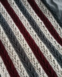 a crocheted blanket is laying on top of a bed sheet with red, white and gray stripes