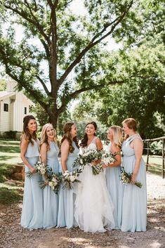 a group of women standing next to each other in front of a tree and house