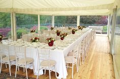 a long table set up with white linens and red flowers in vases on top