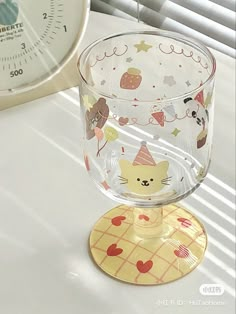 a glass cup sitting on top of a table next to a clock