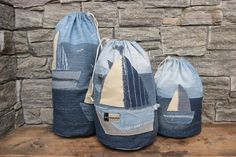 three blue bags with sailboats on them sitting on a wooden shelf in front of a stone wall