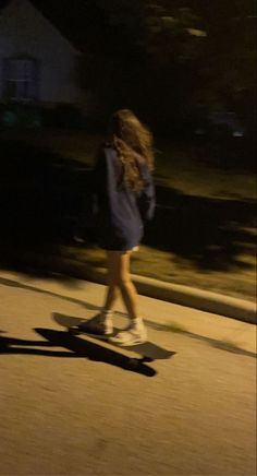 a young woman riding a skateboard down a street at night with her shadow on the ground