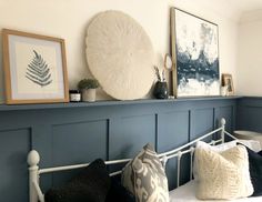 a white bed topped with lots of pillows next to a wall mounted art piece on top of a blue headboard