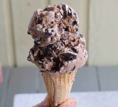 a hand holding an ice cream cone filled with chocolate chip cookies and oreo chunks