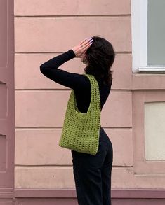 a woman standing in front of a pink building holding a green purse over her head