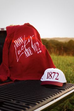 a red shirt and hat sitting on top of a bbq grill in the grass