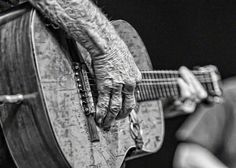 an old person holding a guitar and playing it with their hands in black and white