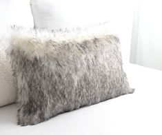 two pillows on a bed with white sheets and fur trimmings, one in grey and the other in light gray