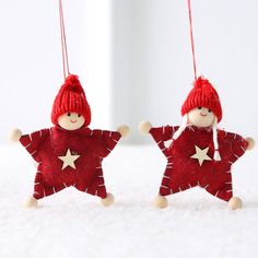 two red felt stars hanging from strings on a white surface, one is wearing a red hat and the other has a star shaped ornament